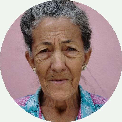 Portrait älterer, sonnengebräunter Frau vor rosa Hintergrund.