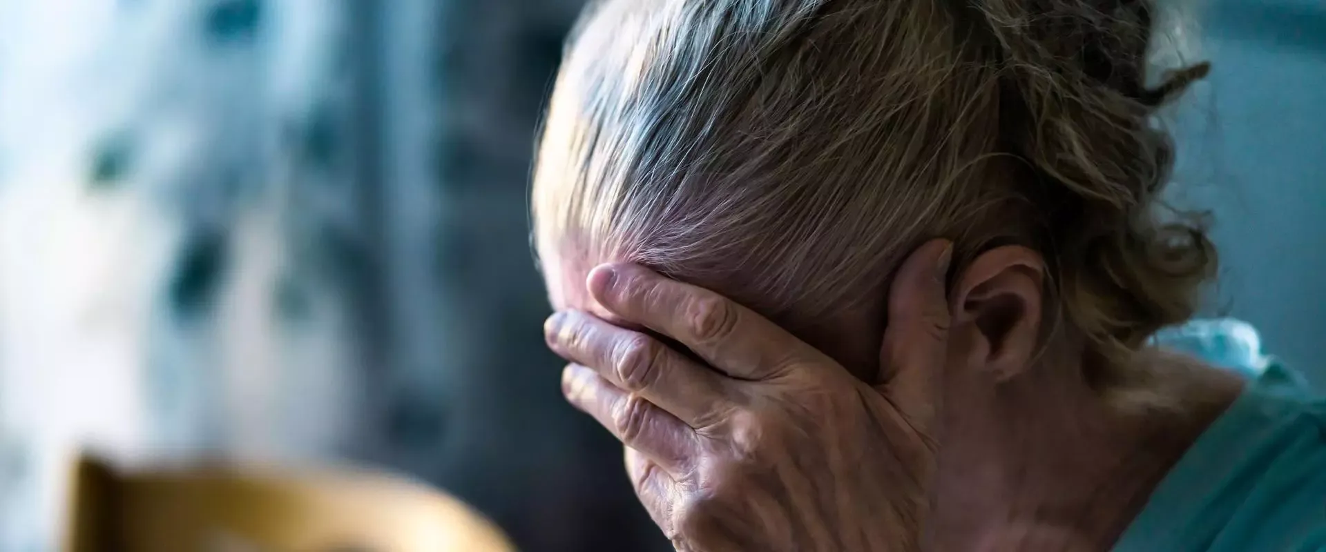 Ältere Frau mit gesenktem Kopf und ihre Hand vor ihr Gesicht haltend.