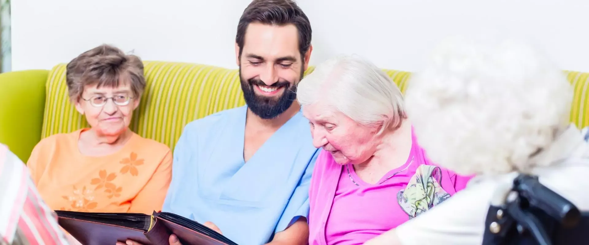 Pfleger sitzt mit Seniorinnen auf einem Sofa