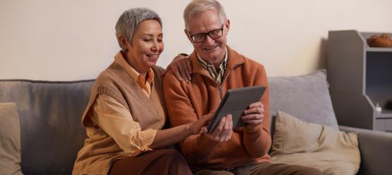 älteres Päärchen sitzt mit einem Tablet auf einem Sofa