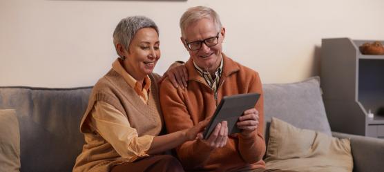 älteres Päärchen sitzt mit einem Tablet auf einem Sofa