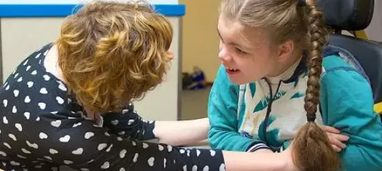 Bild einer Frau die mit einem Mädchem mit Behinderung spricht